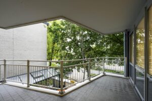 Overdekt balkon met metalen balustrade en uitzicht op bomen aan de Prins Hendrikkade.